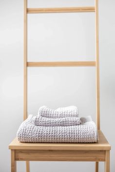 two folded towels sitting on top of a wooden chair next to a white towel rack