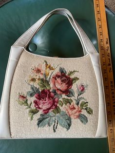 a white purse with flowers on it next to a measuring tape and a green chair