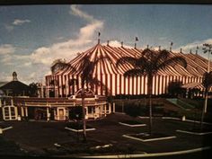 an old photo of a circus tent with palm trees in the foreground and blue sky behind it