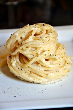 a white plate topped with pasta covered in sauce and seasoning next to a fork