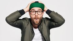 a man with glasses and a green hat covering his ears while standing in front of a white background