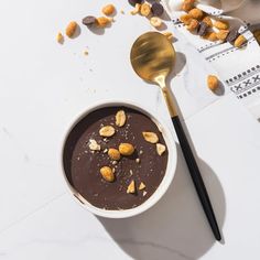 a bowl of chocolate pudding with nuts on top and a spoon next to the bowl