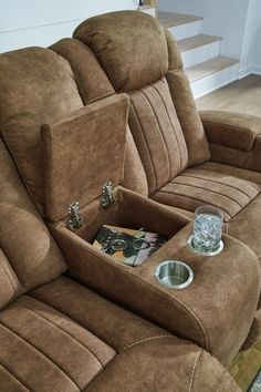 a brown reclining couch with two bowls on it and a magazine in the middle