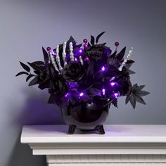 a black vase with purple flowers and candles on a white mantle next to a gray wall