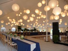 a large tent with tables and chairs set up for a formal dinner or function in white paper lanterns hang from the ceiling