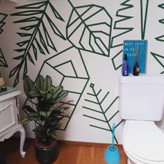 a bathroom with a toilet and a plant in the corner next to it on top of a hard wood floor