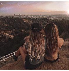 two women sitting on top of a hill looking at the city