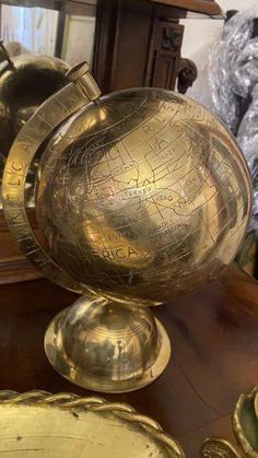 an antique globe is on display in front of other brass plates and bowls, including one for sale