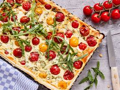 a pizza with tomatoes, cheese and herbs on it next to a knife and fork