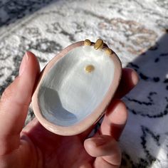 a hand holding a small white shell with tiny gold studs on it