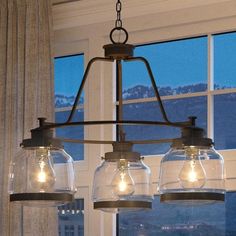 three lights hanging from a chandelier in front of a window with mountains outside