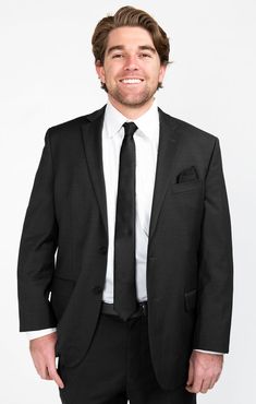 a man in a black suit and white shirt is smiling at the camera with his hands in his pockets