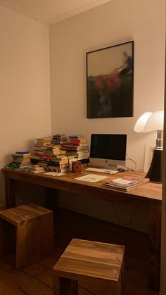 a wooden desk topped with a laptop computer next to a pile of books on top of a hard wood floor