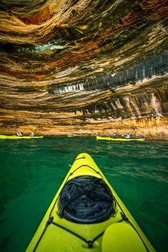 two kayakers paddling through the water in front of cliffs