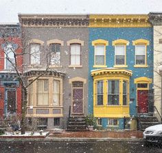 a row of multi - colored houses on a snowy day in the winter with snow falling