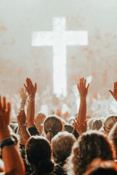 many people are raising their hands in front of a cross