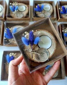 a hand holding a glass box filled with blue feathers and other items on top of it