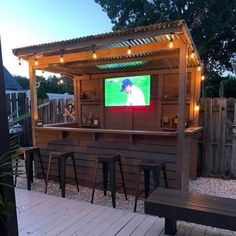 an outdoor bar with stools and a television on the wall in front of it