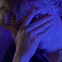 a man covering his face with his hands while sitting in front of a purple light