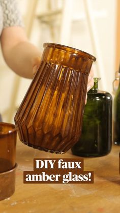 a person holding a brown glass vase with the words diy faux amber glass on it