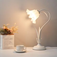 a white table lamp next to a cup and saucer