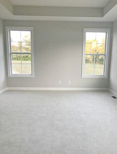 an empty room with two windows and carpet