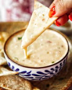 a person dipping tortilla chips into a bowl of quesadilla dip