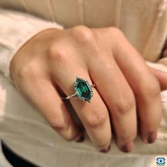 a close up of a person's hand wearing a ring with an emerald stone