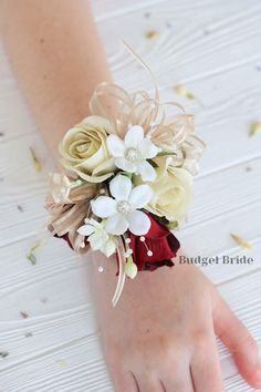 a woman's hand holding a wrist corsage with white and red flowers