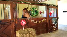 a horse in a stall with hay and christmas decorations on the wall behind it,