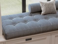 a blue and white checkered couch sitting in front of a window with two pillows on it