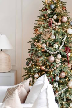 a decorated christmas tree in a living room next to a white couch with pillows on it