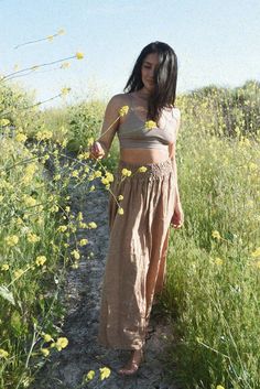 a woman standing in the middle of a field with wildflowers on her side