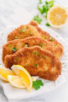 three fried fish fillets on a plate with lemons and parsley