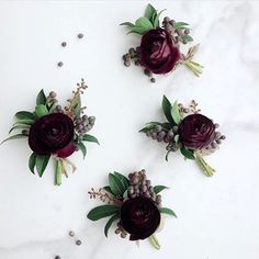 three purple flowers are arranged on a white marble surface with green leaves and berries in the center