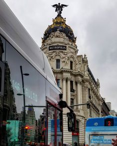 a double decker bus driving down the street in front of a tall building with a statue on top