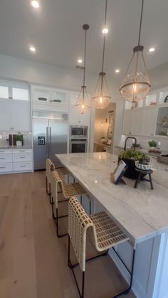 a kitchen with white cabinets and marble counter tops, lights hanging from the ceiling over the island