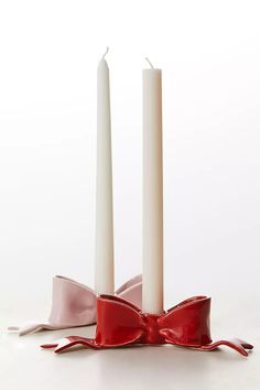 two white candles with red bows on them sitting in front of a candle holder that has pink ribbon tied around it