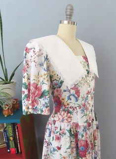 Vintage cottagecore dress from the 70's era! Colorful cabbage rose floral print in red, green, and blue. V-neck with removable panel, short pleated sleeves with buttons, puffed shoulders, and large white lace trimmed prairie collar. Button up front bodice, v-shaped gathered low waist with midi length full skirt. Removable shoulder pads. Step in and button front. Perfect for a spring party! Fits like a modern medium. Please check the measurements below: MEASUREMENTS--Taken with garment laying fla Cottagecore Floral Prairie Dress For Summer, Spring Floral Print Fitted Prairie Dress, Short Sleeve Prairie Dress For Spring Garden Party, Spring Cottagecore Vintage Dress With Short Sleeves, Cottagecore Vintage Short Sleeve Dress For Spring, Fitted Floral Print Dress With Collar, Vintage Floral Print Short Sleeve Prairie Dress, Vintage Short Sleeve Prairie Dress With Floral Print, Cottagecore Prairie Dress With Ditsy Floral Print For Spring