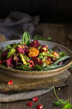 a bowl filled with salad on top of a wooden table next to pomegranates