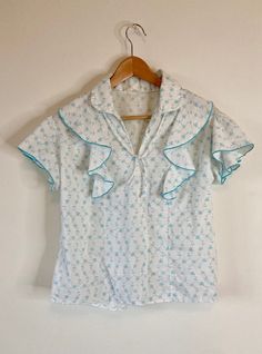 "Lovely vintage cotton blouse from the 1970s. White and turquoise floral pattern with ruffles on sleeves and neckline. Neckline also has a very small tie.  BRAND / LABEL: No tag CONDITION: Great vintage condition, no stains, no holes  ✂ - - - MEASUREMENTS: Measurements are taken laying flat and doubling for a close approximation(in inches): Approx. Women's Medium Shoulder seam to shoulder seam: 17\" Shoulder to hem: 22\" Bust: 41.5\" Waist: 40\"" Cotton Blouse With Vintage Print, Retro Tops With Ruffled Collar For Daywear, Retro Cotton Tops With Ruffles, Retro Cotton Tops With Ruffled Collar, Retro Ruffled Blouse For Vintage Fashion, Vintage Ruffled Blouse For Daywear, Vintage Ruffles Blouse For Daywear, Vintage Tops With Ruffled Collar, Cotton Vintage Blouse With Vintage Print