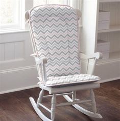 a white rocking chair with pink and grey chevrons on the back, sitting in front of a window