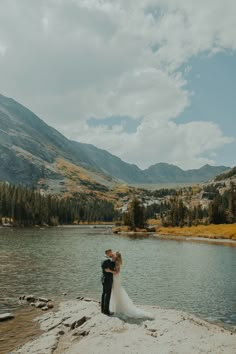 a bride and groom standing on the edge of a lake