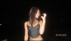 a woman in a black bra top is standing outside at night with her hand up to her face