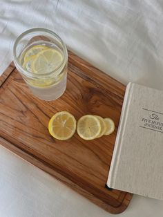 two slices of lemon sitting on top of a wooden cutting board next to a glass of water