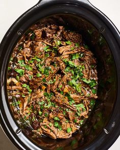 a slow cooker filled with meat and vegetables on top of a white countertop