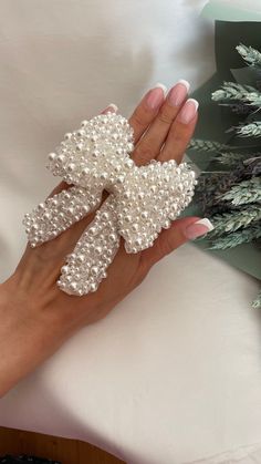 a hand holding a fake white snowflake on top of a table next to a christmas tree