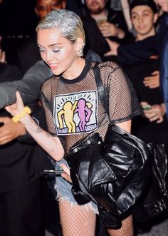 a woman in fishnet shirt and jeans holding a handbag while standing next to other people