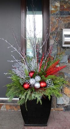 a planter filled with red and silver ornaments on top of a stone floor next to a door