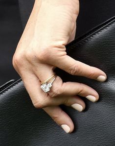 a woman's hand with a ring on her finger holding onto a black purse